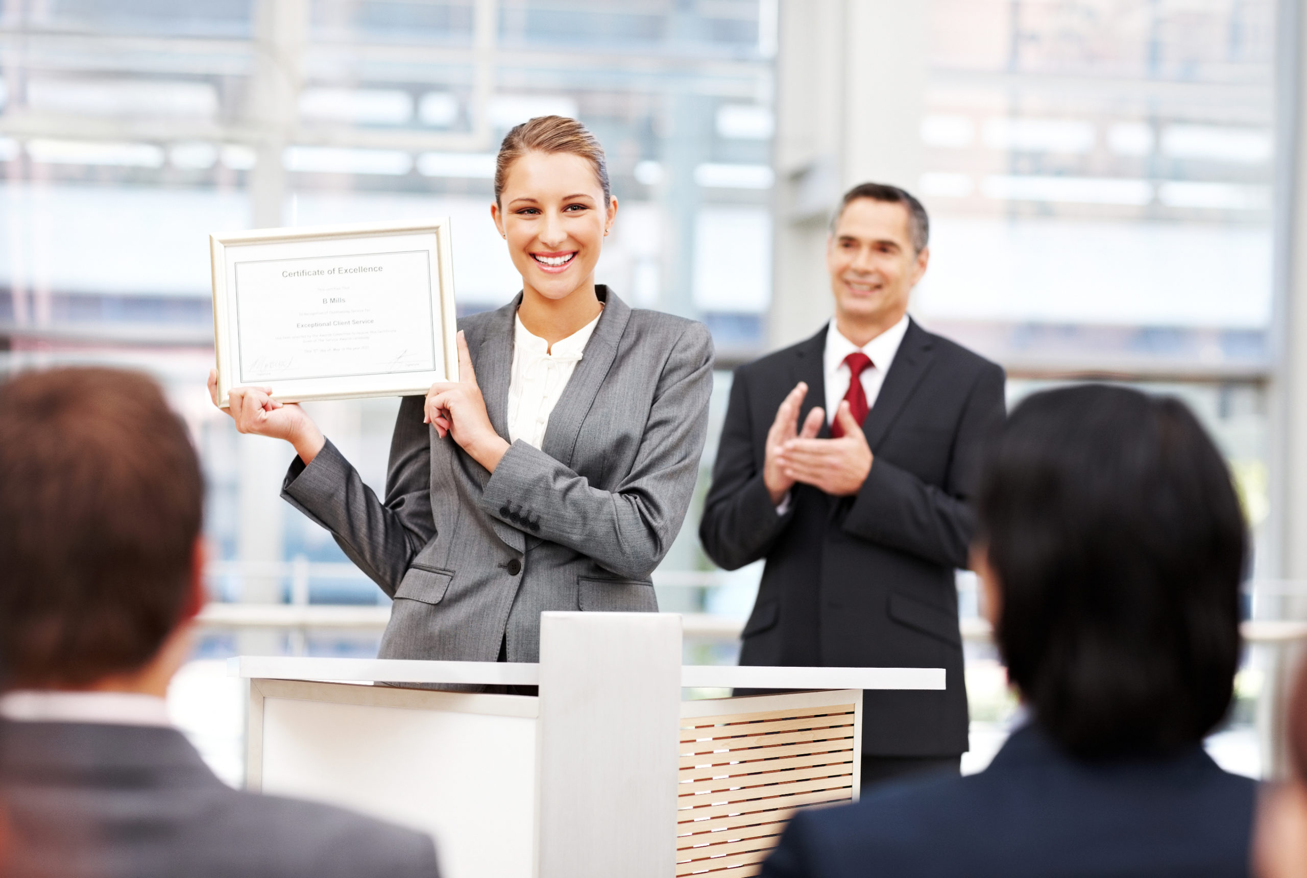 Businesswoman stands up on stage and shows off an award. Horizontal shot.