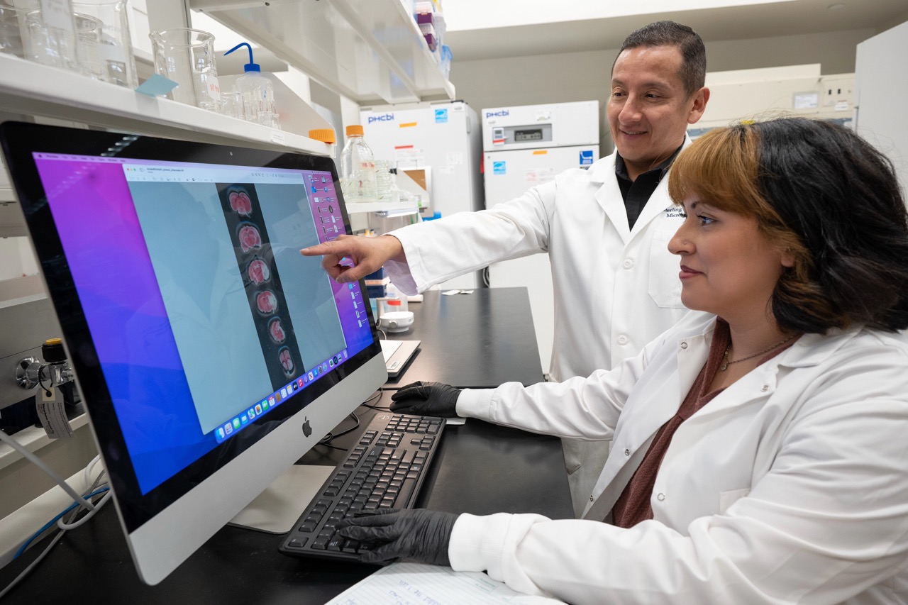 student and faculty member in white lab coats reviewing information on a computer monitor