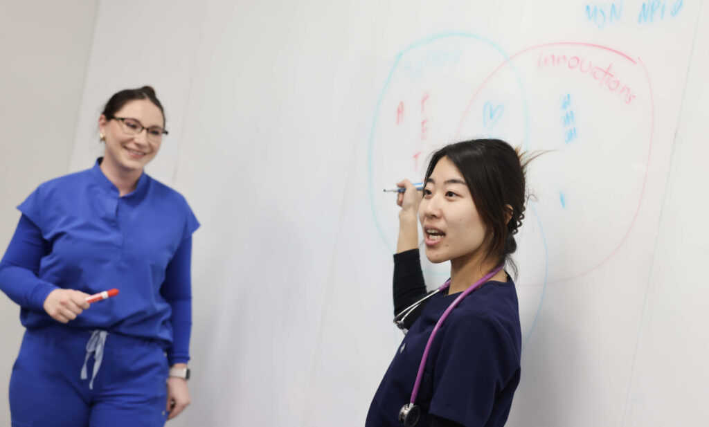 Nursing students work together on a project using a whiteboard.