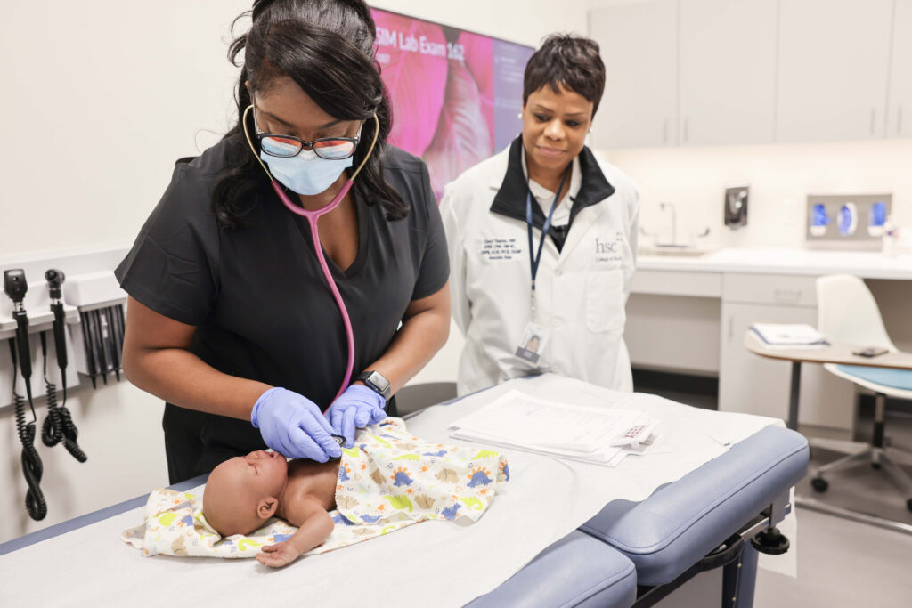 Dr. Cheryl Thaxton observes a nursing student using a stethoscope on an infant mannequin.