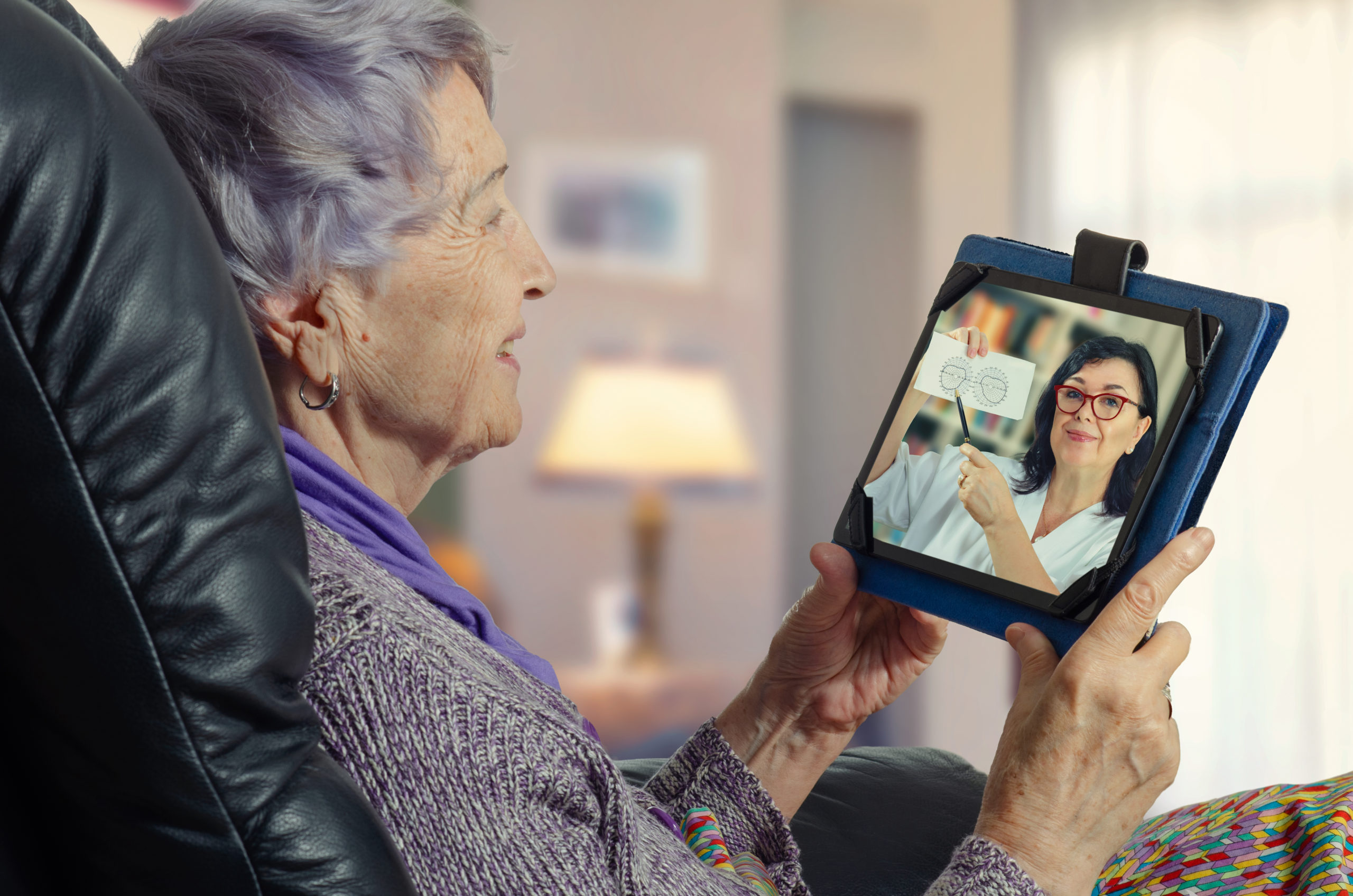 A woman watches a doctor on a screen of a tablet