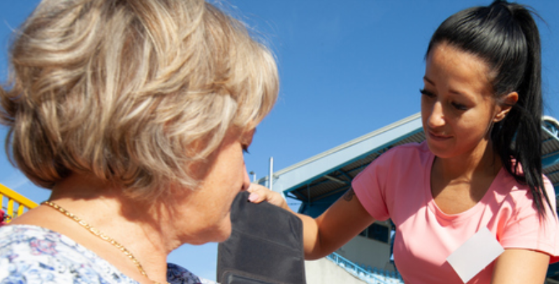 Community health worker placing a blood pressure cuff on a seated woman.