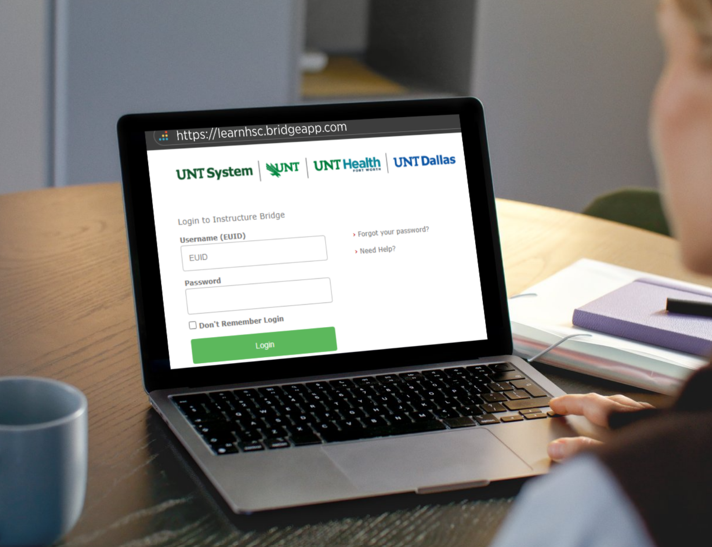 A person is using a laptop displaying the UNT System login page for Instructure Bridge. The screen shows fields for EUID and password.