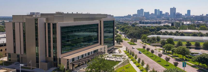 The IREB building with reflective glass windows stands in the foreground, surrounded by greenery. The city skyline is visible in the distance under a clear blue sky.