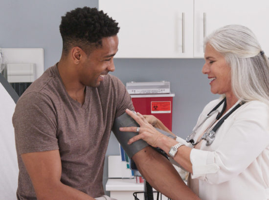 Mature White Female Physician Checking Male Patients Blood Pressure At Clinic